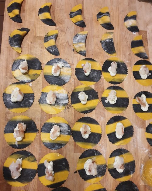 A wooden surface covered with yellow and black pasta shapes, some topped with small pieces of seafood.