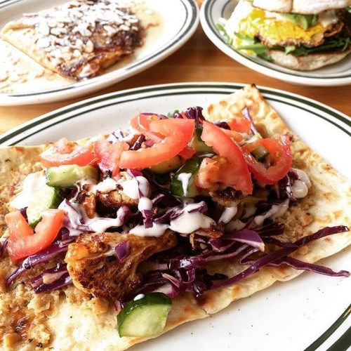 A flatbread topped with grilled chicken, red cabbage, tomatoes, cucumbers, and drizzled with sauce.