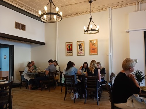 A cozy restaurant interior with diners at wooden tables, vintage posters on the walls, and warm lighting.
