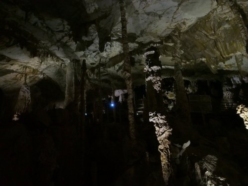 Dimly lit cave interior with stalactites and stalagmites, showcasing unique rock formations and shadows.