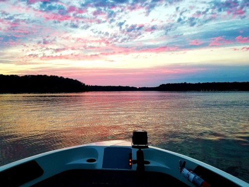 A serene view from a boat at sunset, with vibrant pink and purple clouds reflecting on the calm water.