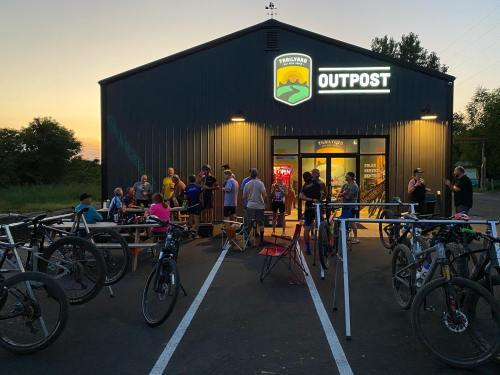 A group of people socializing outside a bike shop at sunset, with bicycles parked nearby.