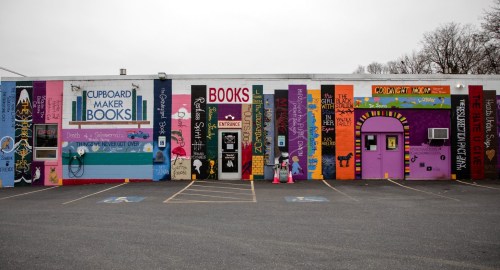 Colorful mural on a building featuring book titles and playful designs, with a purple entrance and various artistic elements.