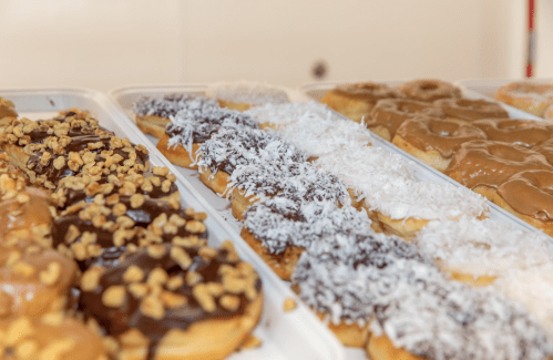 A variety of donuts topped with chocolate, coconut, and nuts, displayed on a tray.