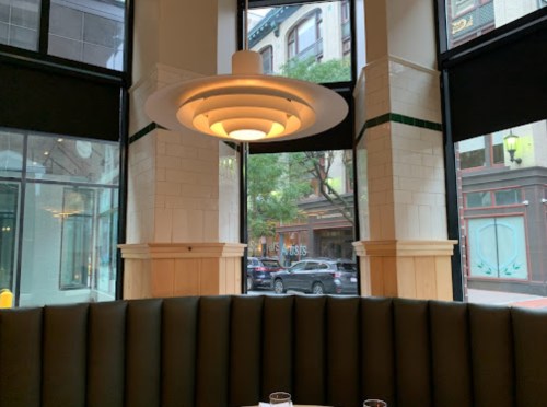 A modern restaurant interior featuring a unique pendant light and large windows overlooking a city street.