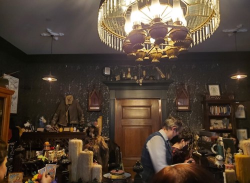 A dimly lit shop interior with vintage decor, featuring a chandelier and shelves filled with various items.