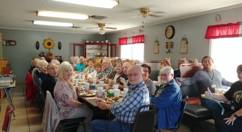 A large group of people sitting at a long table in a cozy dining room, enjoying a meal together.