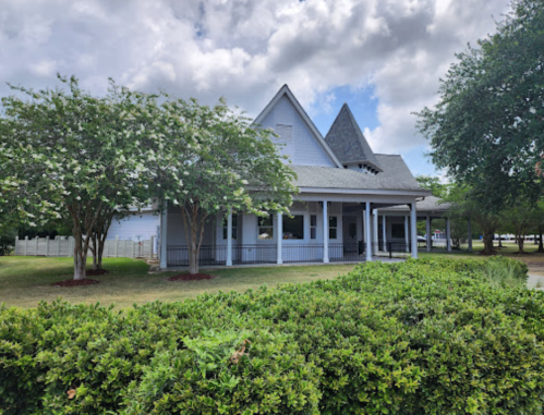 A charming blue house with a steep roof, surrounded by green bushes and trees under a partly cloudy sky.