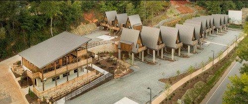 Aerial view of a modern cabin complex with multiple A-frame cabins and a central lodge surrounded by greenery.