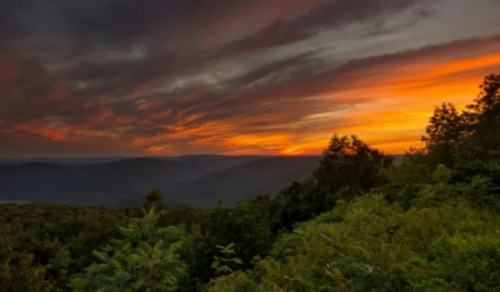 A vibrant sunset over rolling hills, with dramatic clouds and lush greenery in the foreground.