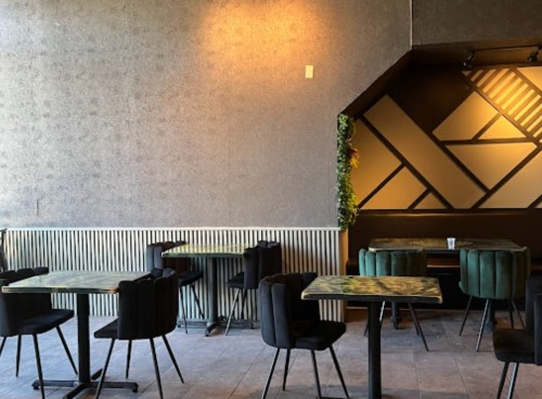 A modern café interior with green velvet chairs, patterned walls, and empty tables in a cozy atmosphere.