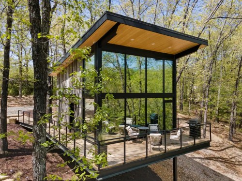 Modern glass house nestled among trees, featuring a spacious deck and contemporary design.