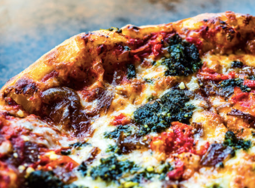 Close-up of a freshly baked pizza topped with melted cheese, herbs, and red toppings on a golden crust.