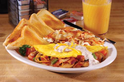 A plate of breakfast featuring an omelet with vegetables, toast, hash browns, and a glass of orange juice.