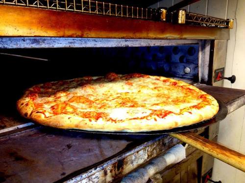 A large, freshly baked pizza with melted cheese and pepperoni, resting on a pizza peel in an oven.