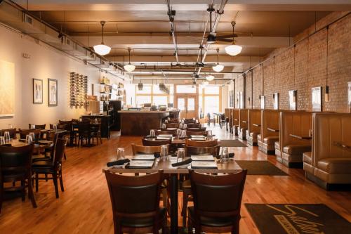 A spacious restaurant interior with wooden tables, booths, and warm lighting, featuring a bar area in the background.