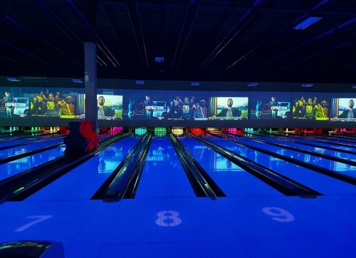 A vibrant bowling alley with glowing lanes and large screens displaying images of bowlers in action.