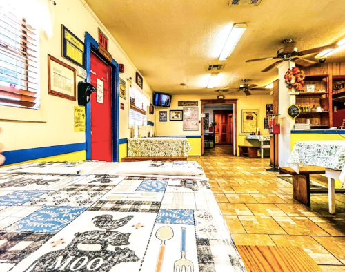 Cozy restaurant interior with checkered tablecloths, colorful walls, and wooden decor, featuring tables and a welcoming atmosphere.