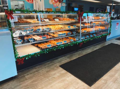 A display case filled with various donuts and pastries, decorated with festive garlands for the holidays.