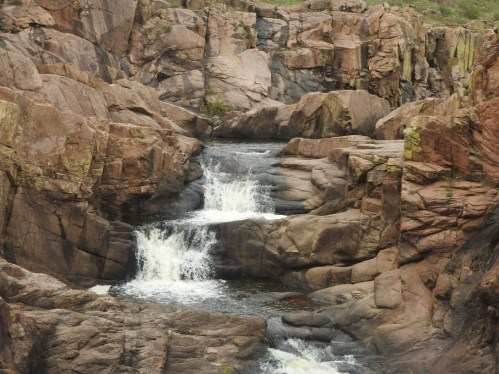 A serene waterfall cascading over rocky terrain, surrounded by rugged cliffs and lush greenery.