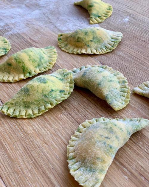 Freshly made green pasta dumplings arranged on a wooden surface, dusted with flour.