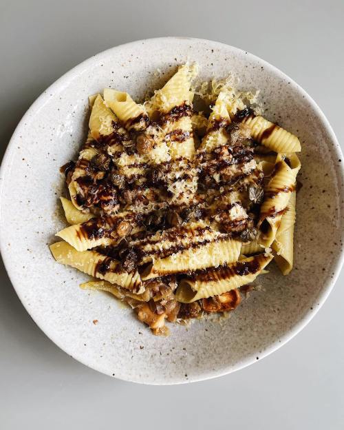 A plate of pasta topped with grated cheese and a drizzle of sauce, served in a speckled bowl.