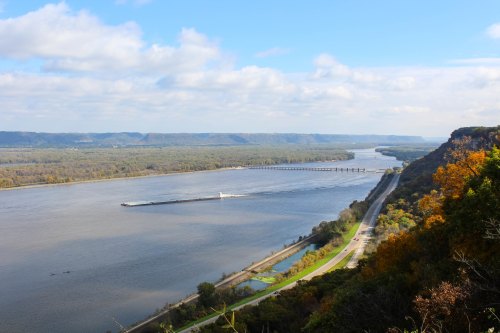 A scenic view of a river winding through green hills, with a barge traveling along the water under a blue sky.