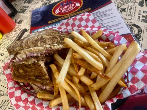 A sandwich with a bite taken out, served with a side of golden French fries in a red and white checkered basket.