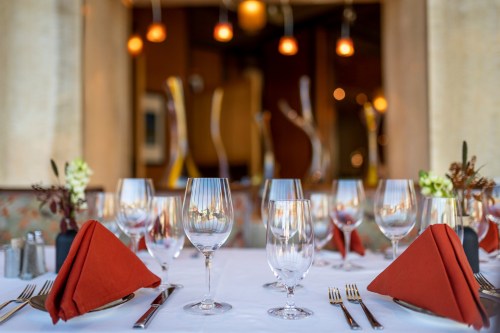 Elegant dining table set with red napkins, glassware, and silverware, with warm lighting in the background.