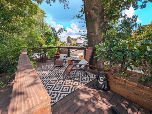 A cozy outdoor deck with two chairs, a small table, and greenery, surrounded by trees and a blue sky.