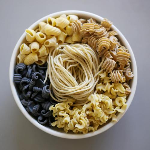 A bowl filled with various types of pasta in different colors and shapes, including spirals and tubes.