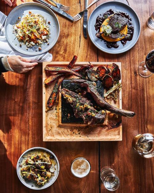 A wooden table with a large meat platter, sides, and drinks, showcasing a variety of gourmet dishes.