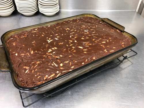 A rectangular pan of chocolate dessert topped with slivered almonds, resting on a wire rack in a kitchen setting.