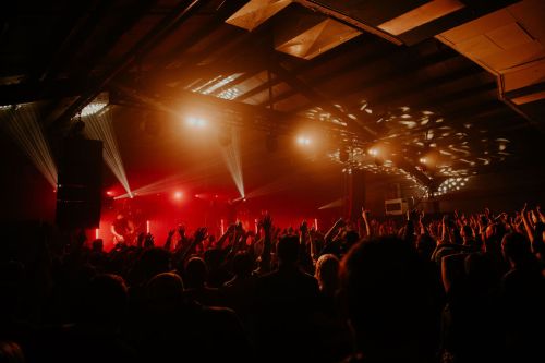 A lively concert scene with a crowd raising their hands, illuminated by colorful stage lights in a dimly lit venue.