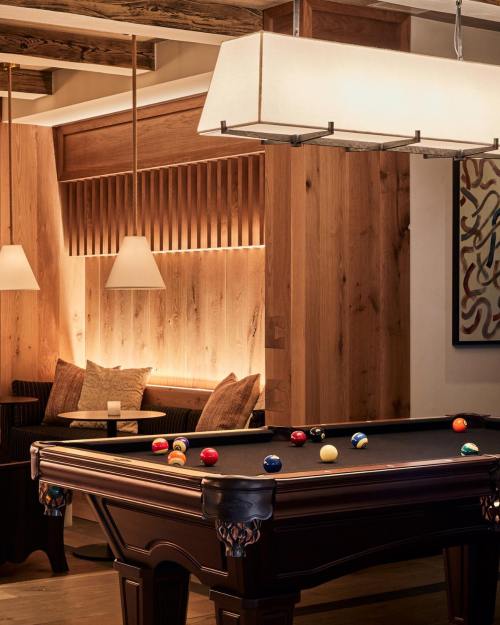 A stylish pool table in a cozy, wooden-paneled lounge with warm lighting and comfortable seating.