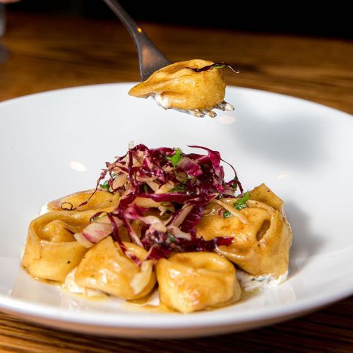 A fork holding a piece of tortellini above a plate of pasta topped with red cabbage and herbs.
