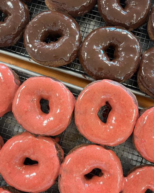 A close-up of assorted donuts: chocolate-glazed and strawberry-glazed, arranged on a cooling rack.