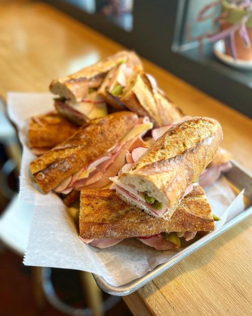 A tray of freshly made sandwiches with layers of meat and pickles, resting on parchment paper.
