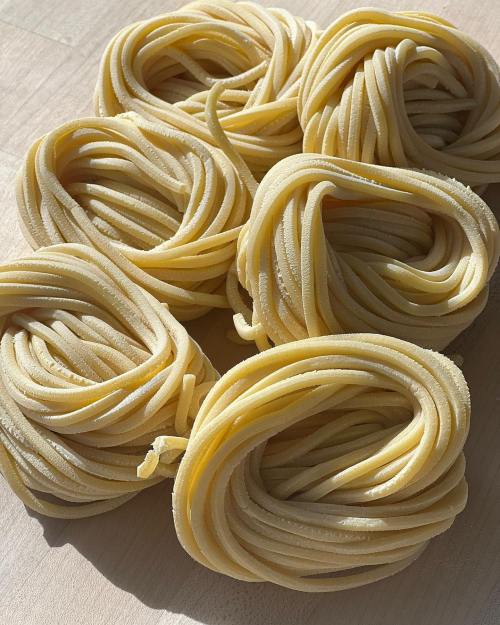 A close-up of several nests of uncooked pasta arranged on a light wooden surface.