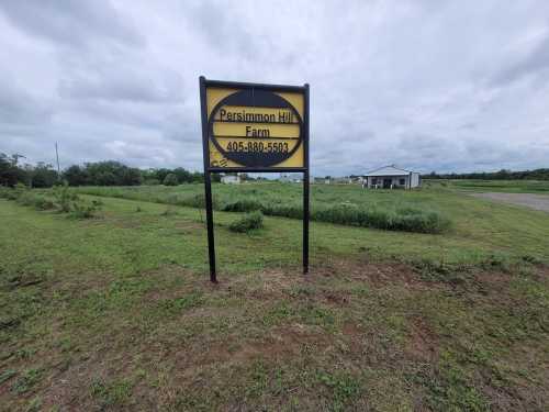 Sign for Persimmon Hill Farm with contact number, set in a grassy area under a cloudy sky.