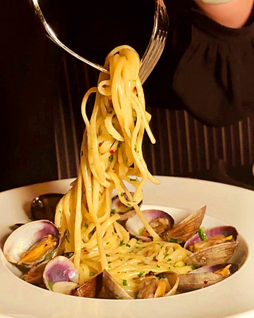 A fork lifting spaghetti with clams in a creamy sauce, garnished with herbs, on a white plate.