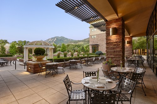 Outdoor dining area with tables and chairs, surrounded by greenery and mountains in the background at dusk.