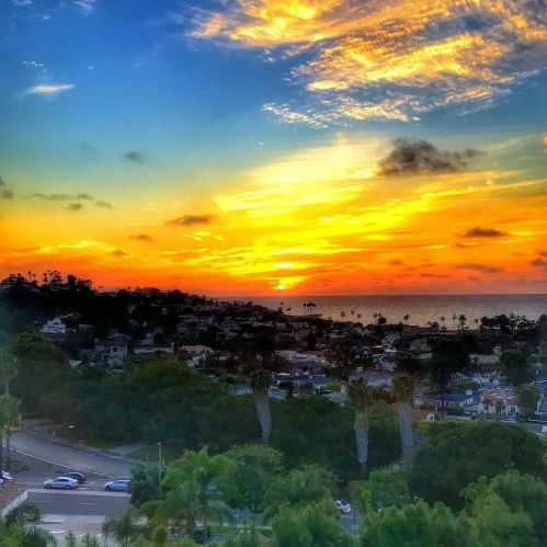 A vibrant sunset over the ocean, with colorful clouds and a view of a coastal town below.