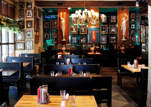 Cozy restaurant interior with wooden tables, framed photos on walls, and a chandelier overhead.
