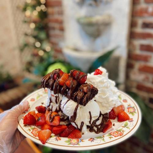 A plate of chocolate-drizzled cake topped with strawberries and whipped cream, surrounded by fresh strawberries.