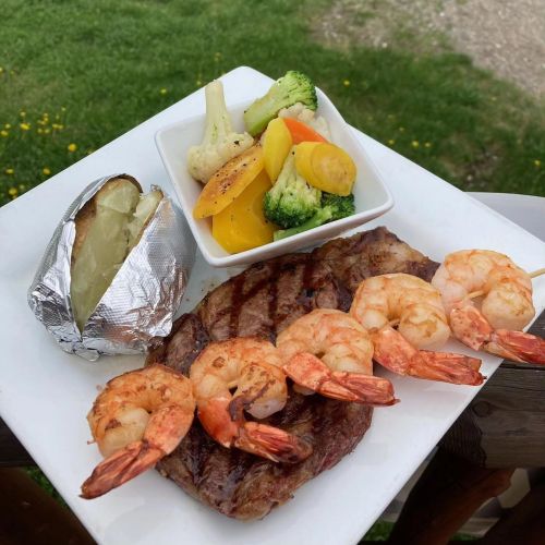 A plate featuring grilled steak, shrimp skewers, a baked potato, and a side of mixed vegetables.