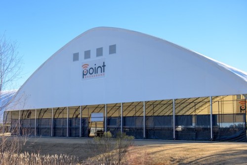 A large, white sports dome with a logo, set against a clear blue sky and grassy area in the foreground.