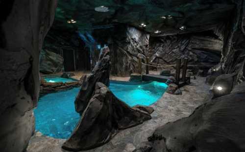 A cave-like indoor pool area with rocky formations and blue water, illuminated by soft lighting.