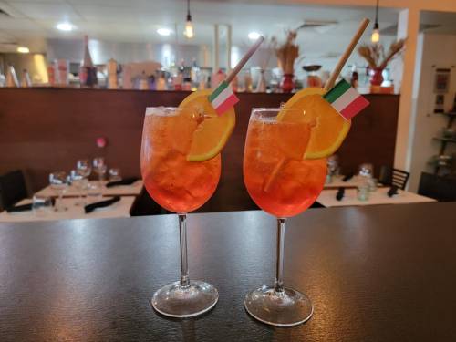 Two cocktails with orange slices and small Italian flags, set against a restaurant background.