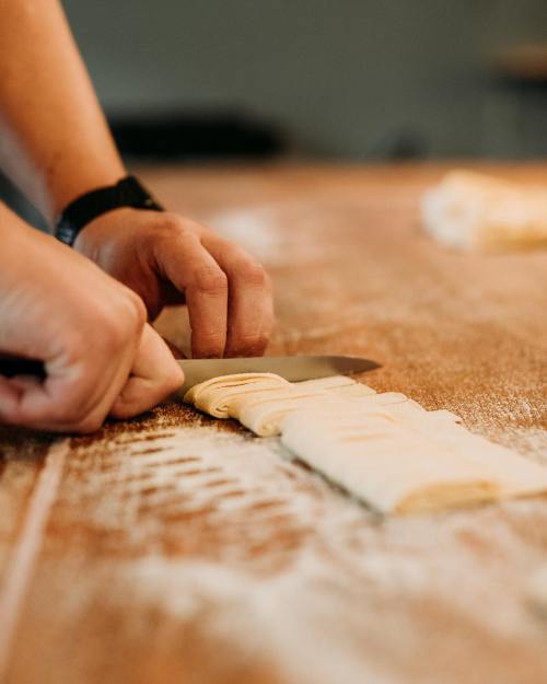 A person’s hands cutting rolled dough on a floured wooden surface with a knife.